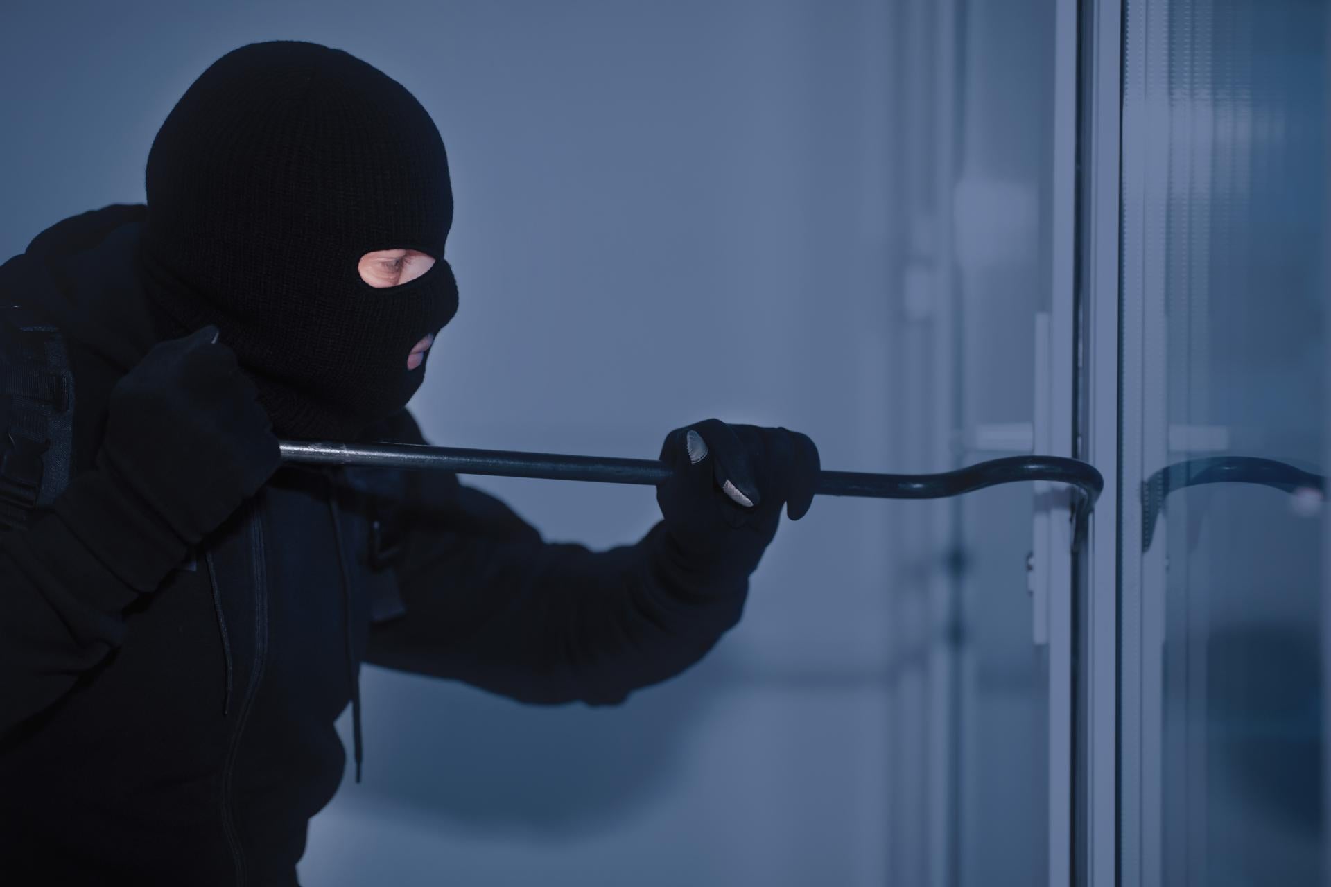 Home Security Concept. Burglar in Action Trying To Break Into the House Using Crowbar, Side View