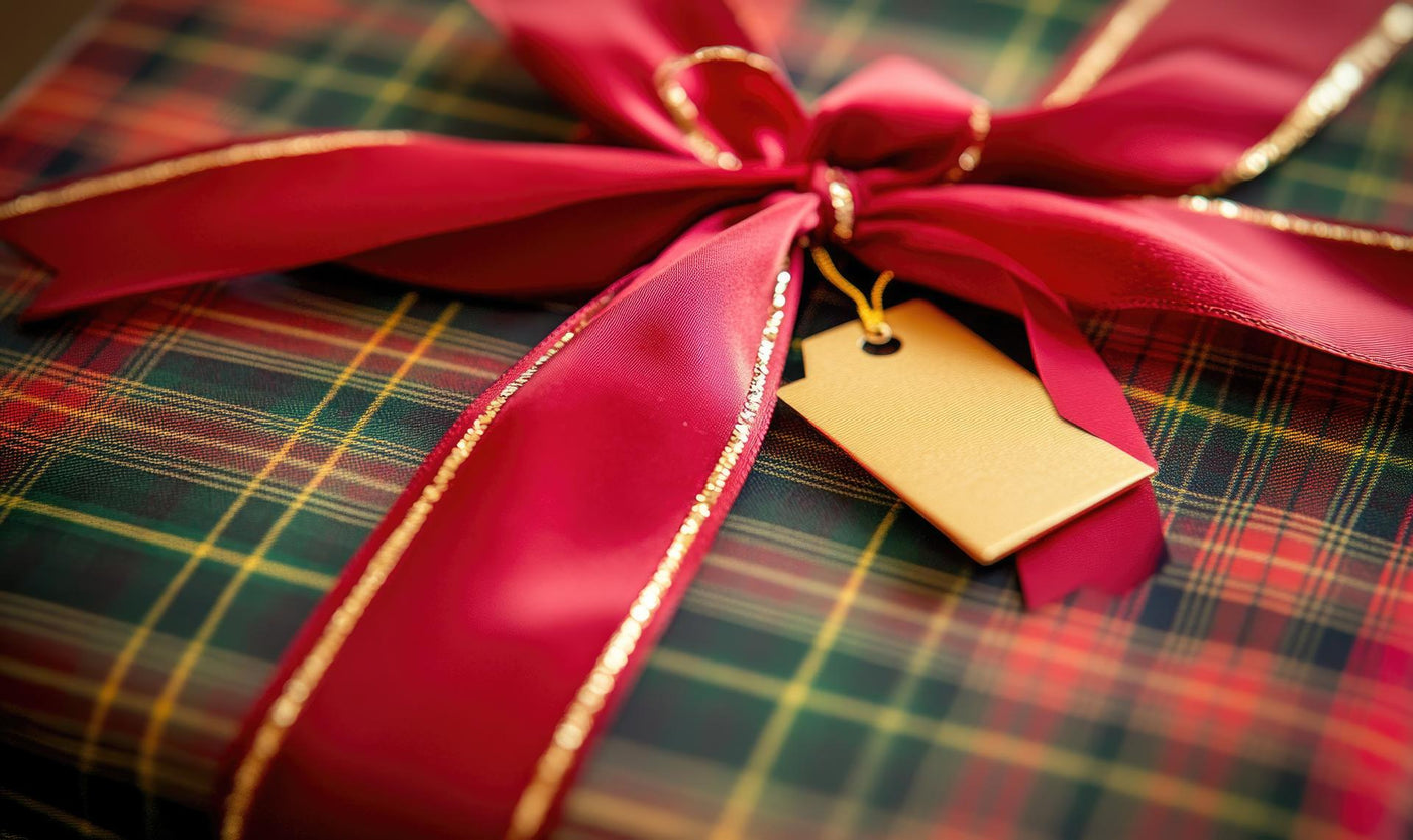 A red and green plaid wrapped gift with a gold ribbon and a yellow tag