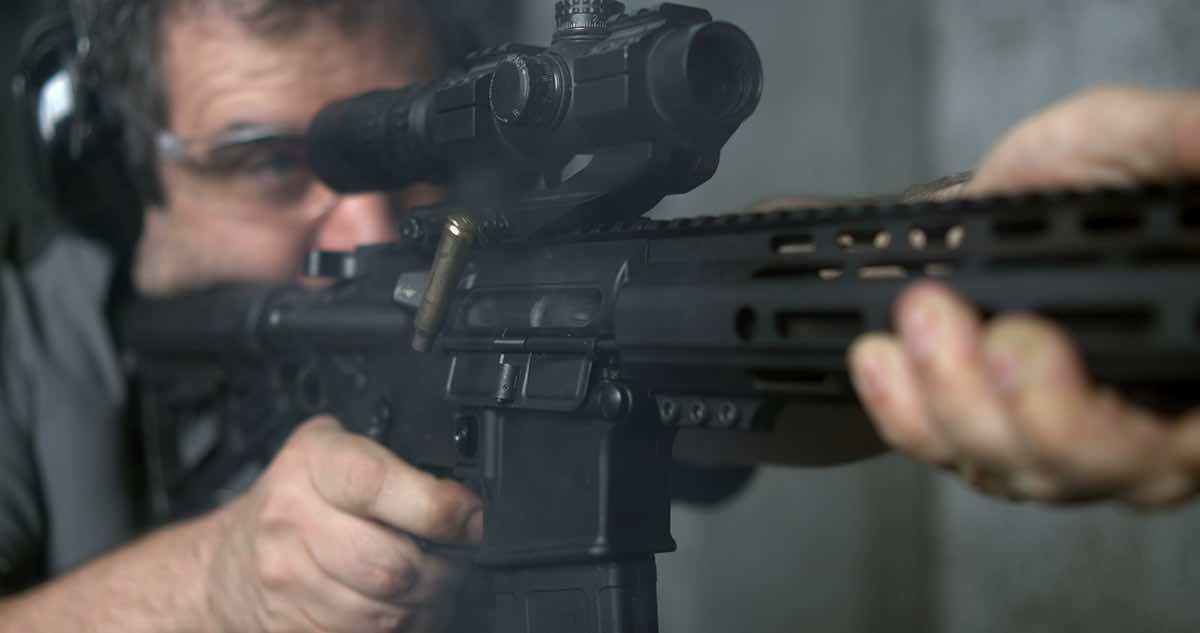 Person aiming a rifle with a scope in a shooting range.