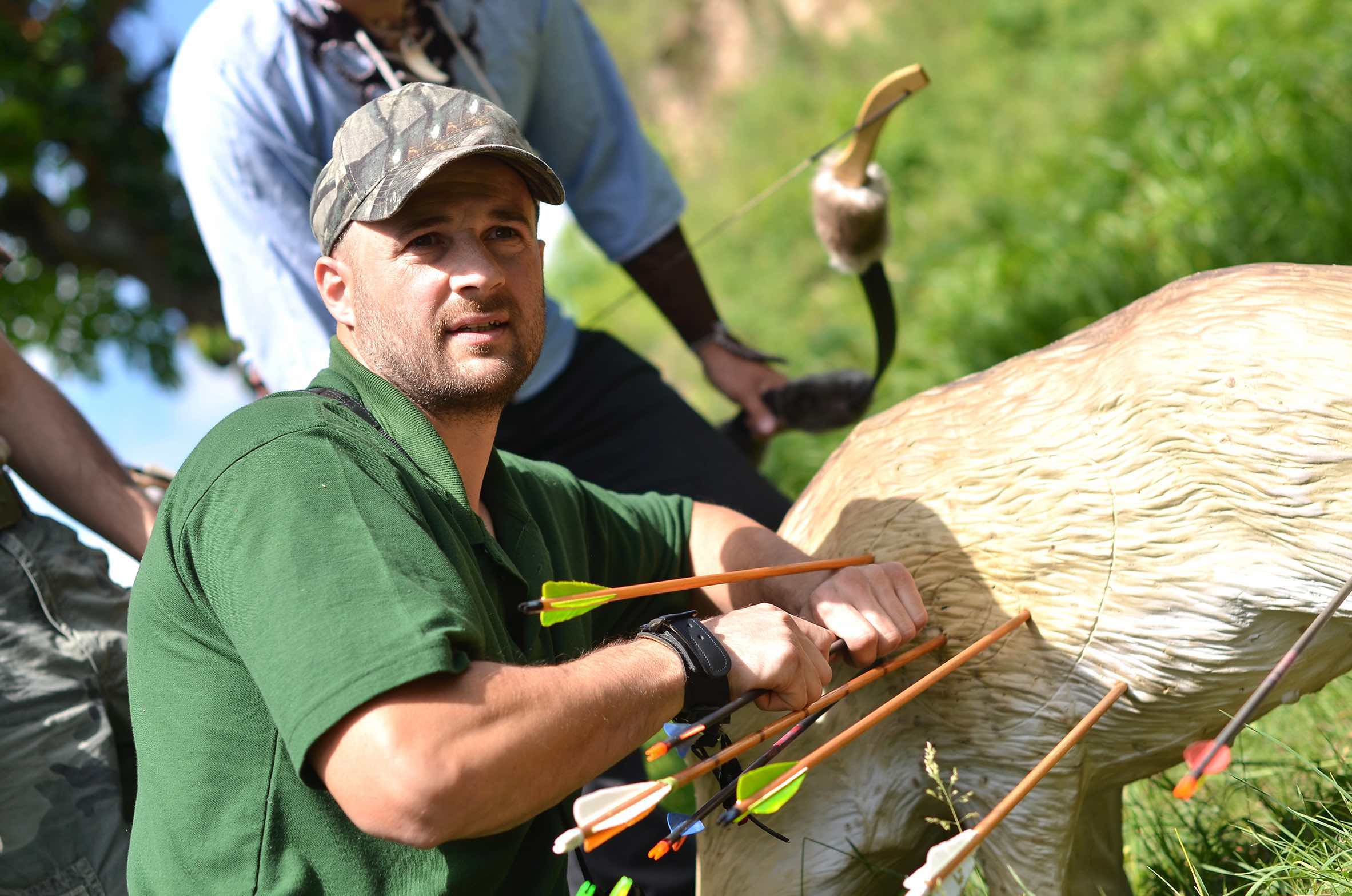 Man in a green shirt placing arrows into a target outdoors.