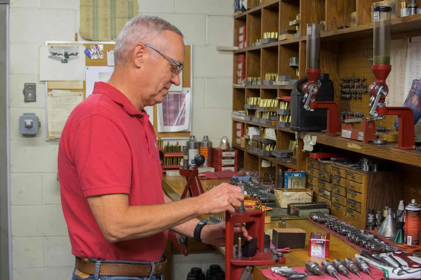 An elderly man working at a cluttered tool bench.