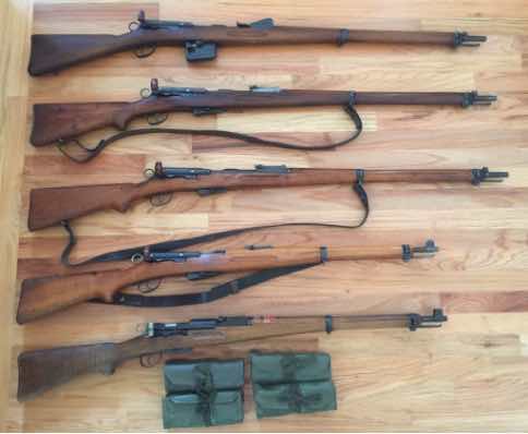 Six rifles arranged on a wooden surface with ammunition clips.