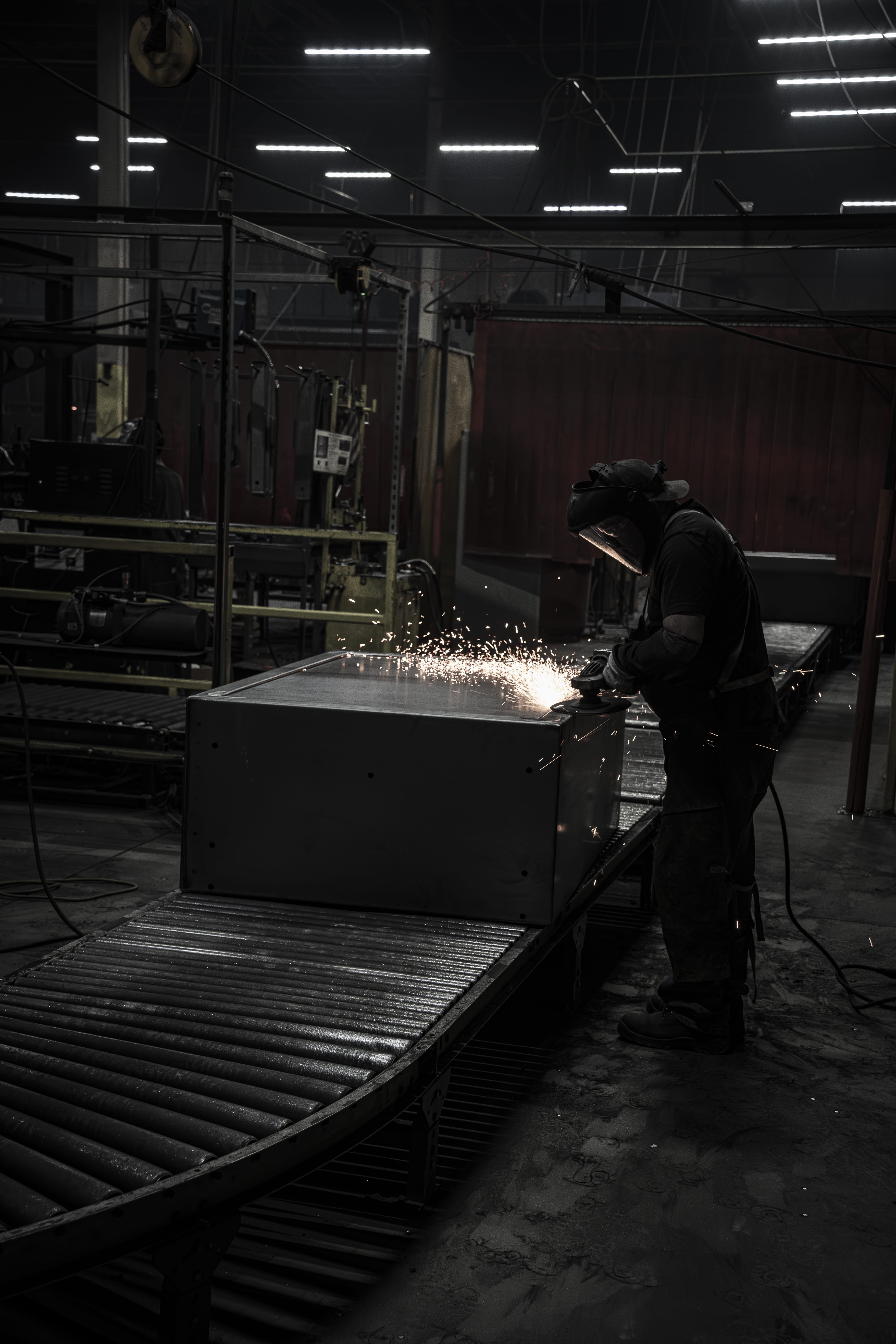 A worker welding metal in a dimly lit industrial setting.