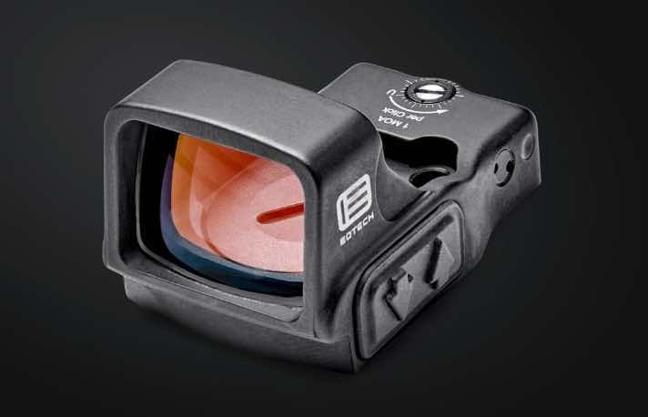 Black reflex sight with a colored lens on a dark background.