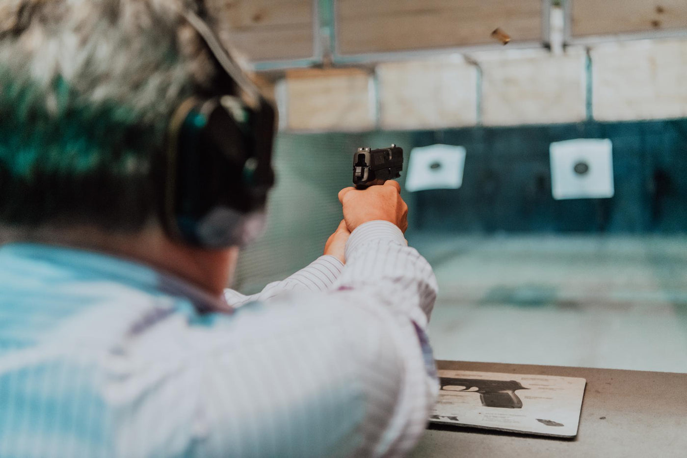 A man practices shooting a pistol in a shooting range while wearing protective headphones