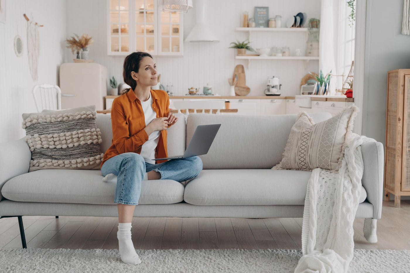 Pensive dreaming female rests with laptop on comfortable modern sofa in cozy living room at home