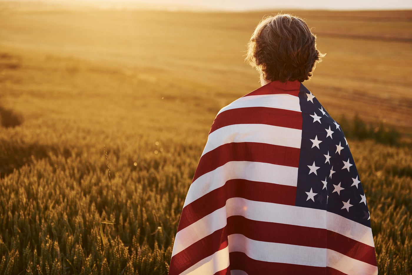 View from behind. Holding USA flag in hands. Patriotic senior stylish man with grey hair and beard on the agricultural field