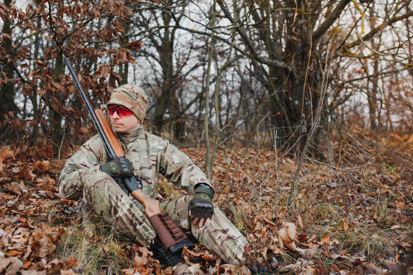 A male hunter with a gun while sitting takes aim at a forest. The concept of a successful hunt, an experienced hunter. Hunting the autumn season. The hunter has a rifle and a hunting uniform