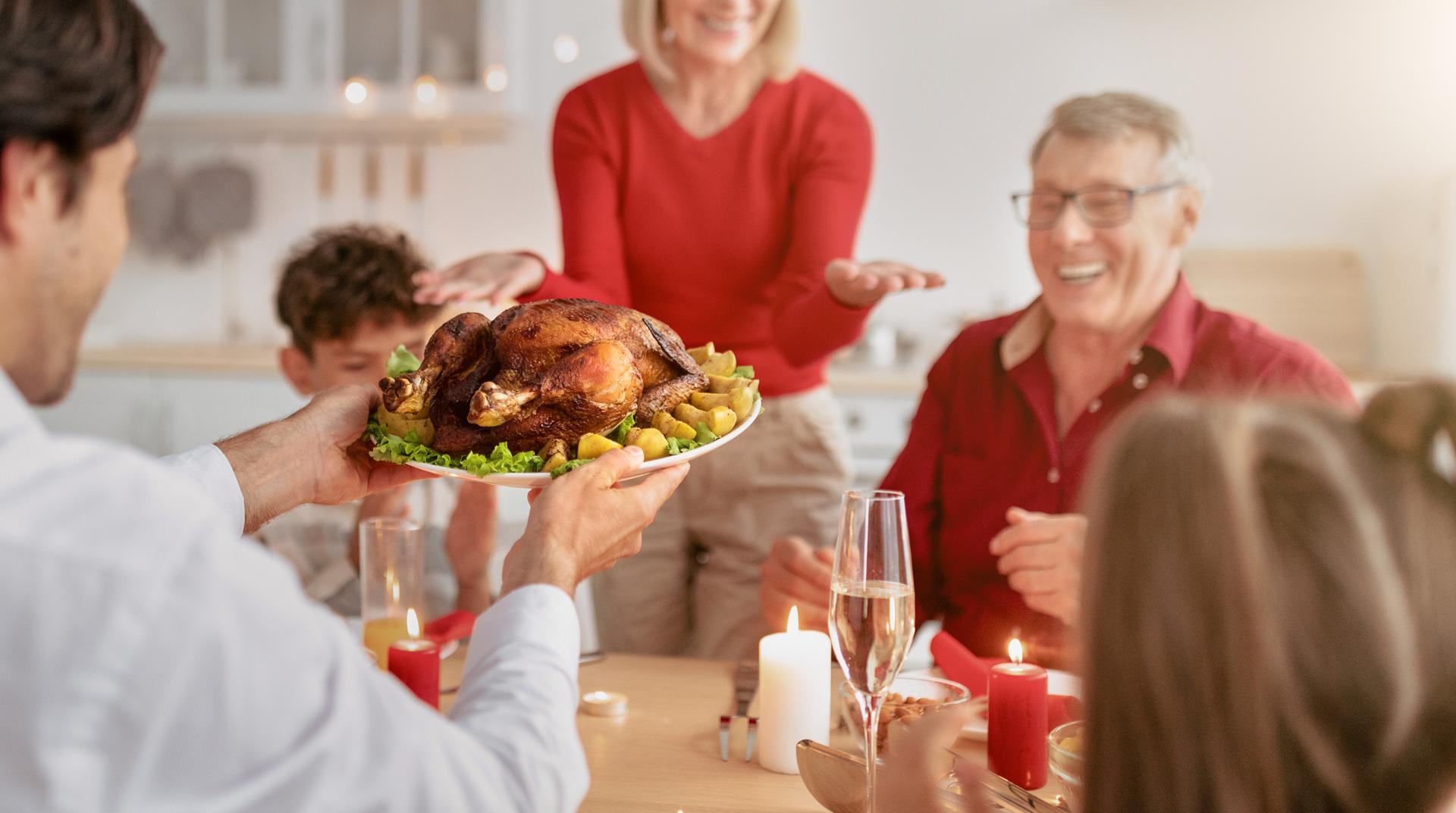 Young man serving traditional holiday turkey for big extended family, celebrating Thanksgiving or Christmas at home, enjoying festive meal with relatives, selective focus. Free space