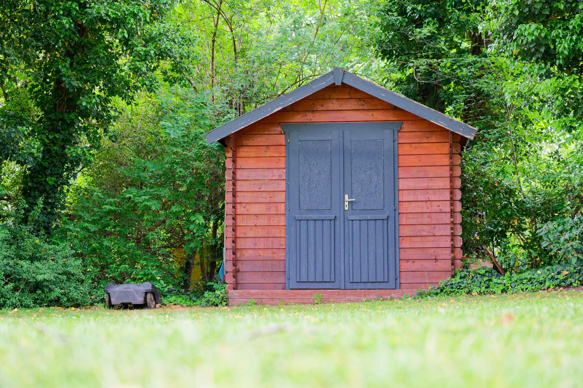 Small storage shed with black full height doors and mower.