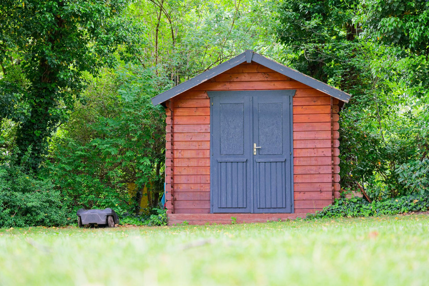 Small storage shed with black full height doors and mower.