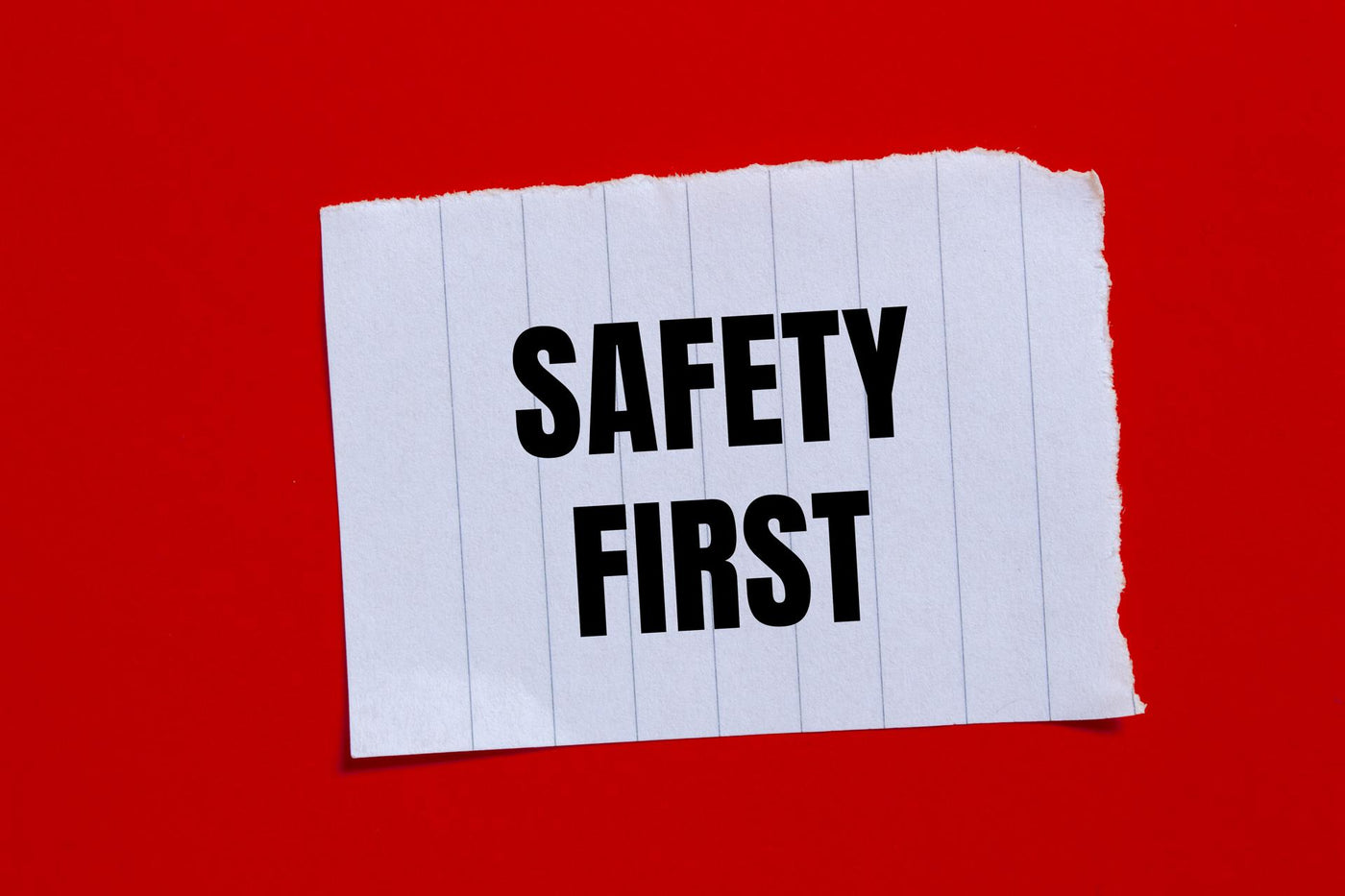Safety first message written on ripped torn paper piece with red background. Conceptual safety first symbol. Copy space.
