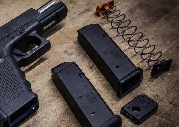 A disassembled handgun with magazines and a spring on a wooden surface.